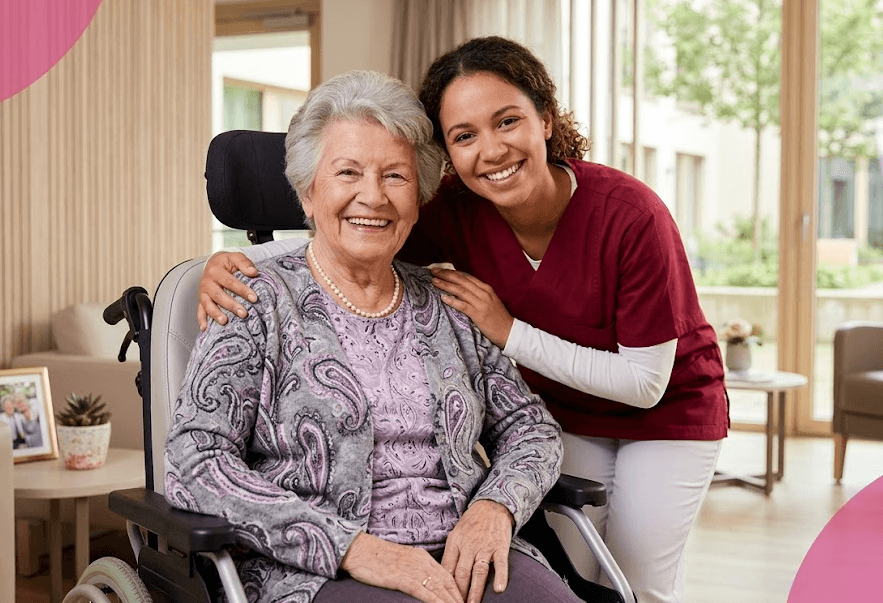 A smiling Namicare support worker with her arm around an older woman in a wheelchair at home